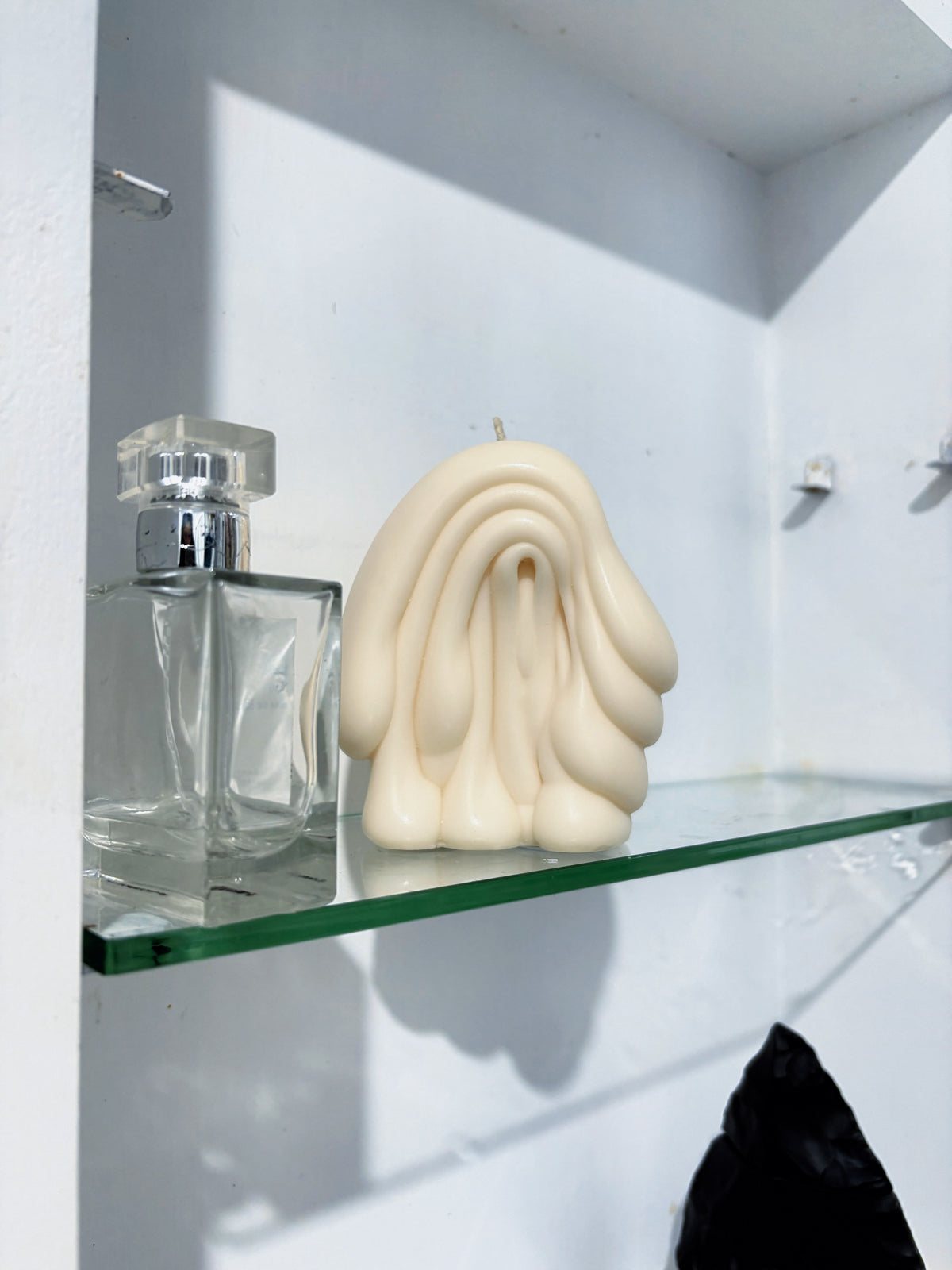 Fold sculptural candle by Post Objects on a glass shelf beside a clear perfume bottle