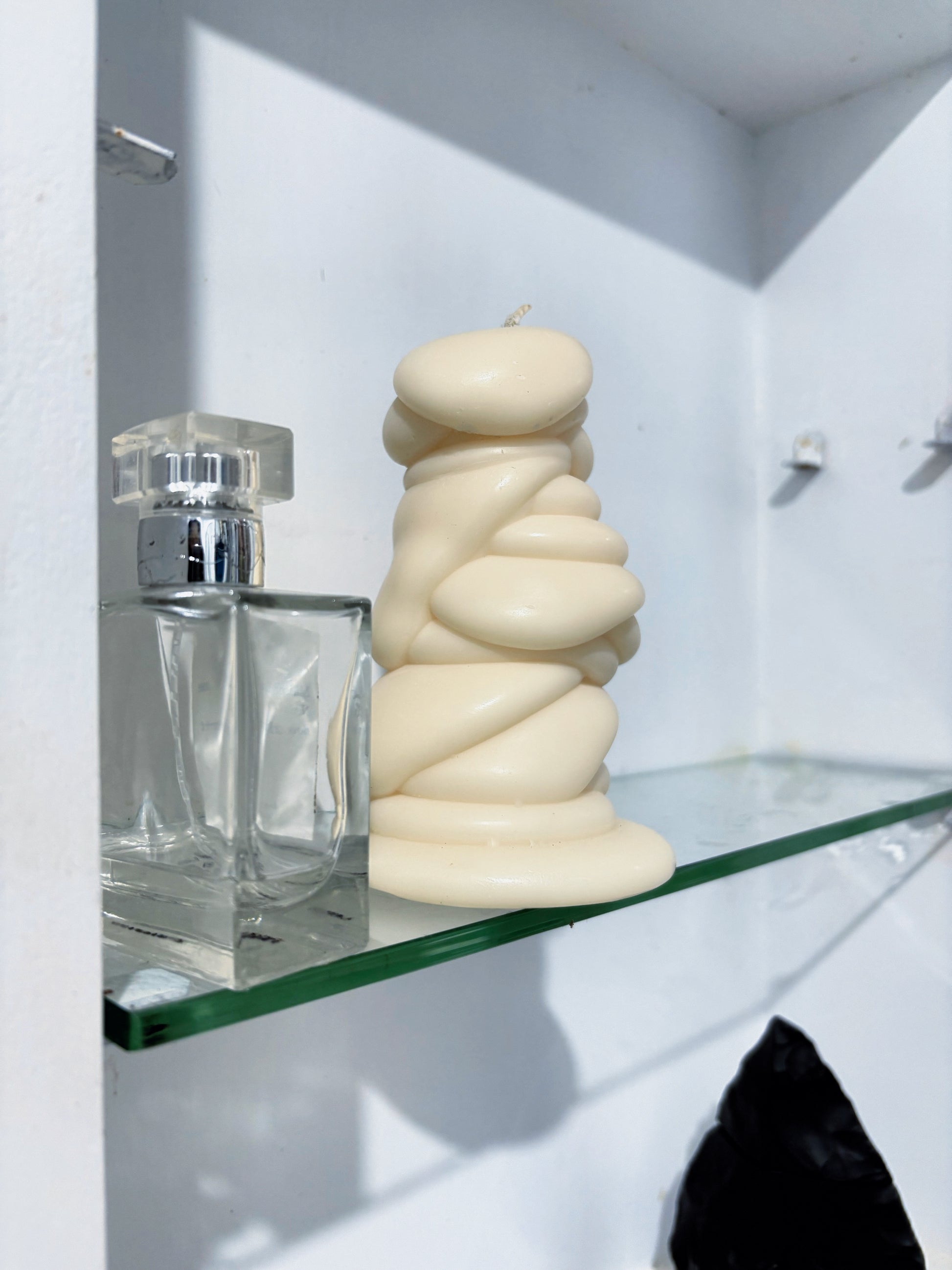 post objects off-white sculptural drip candle displayed on a glass shelf next to a clear perfume bottle 